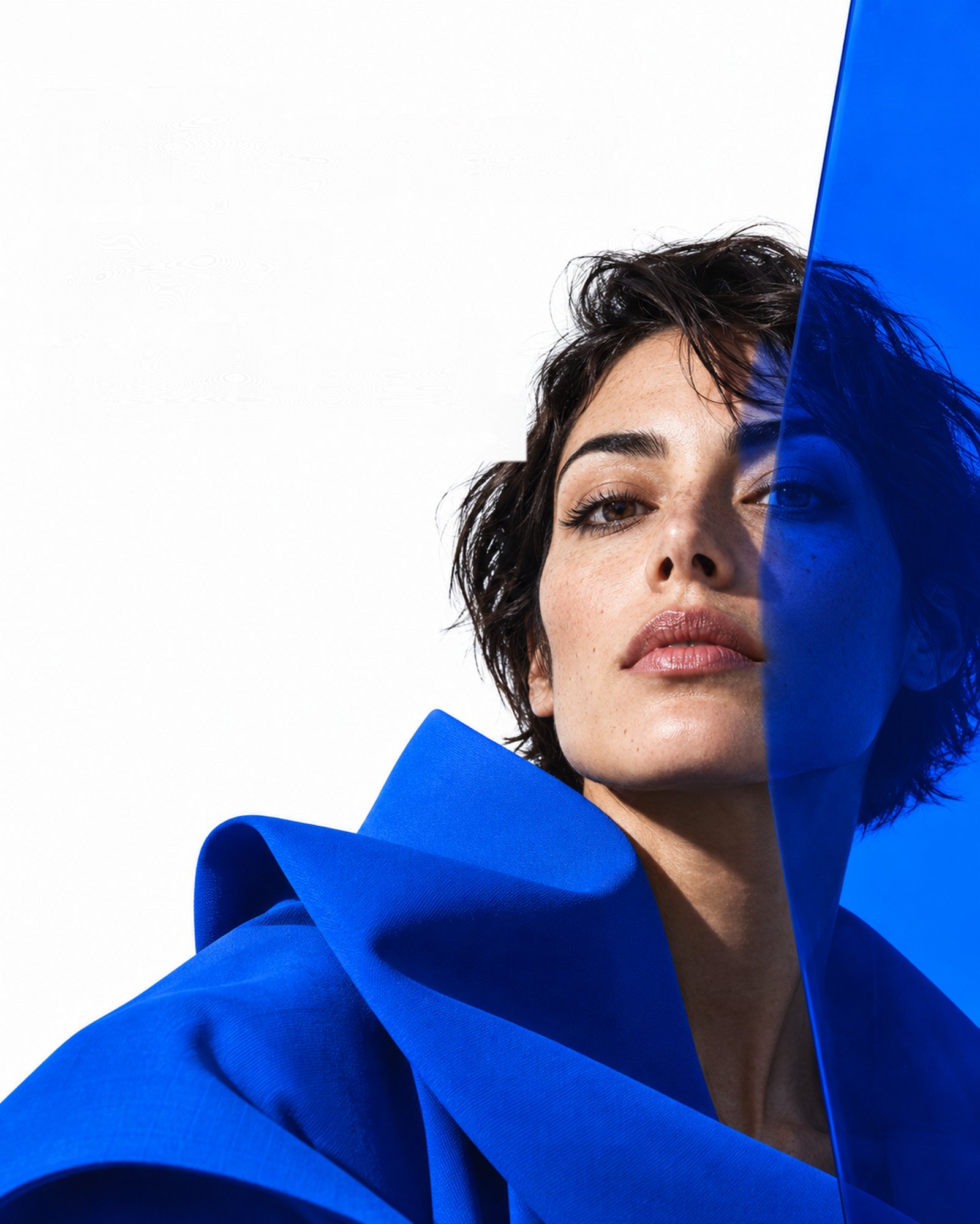Portrait of a woman with short dark hair, half her face behind a sheet of cobalt blue. Illustrative image.